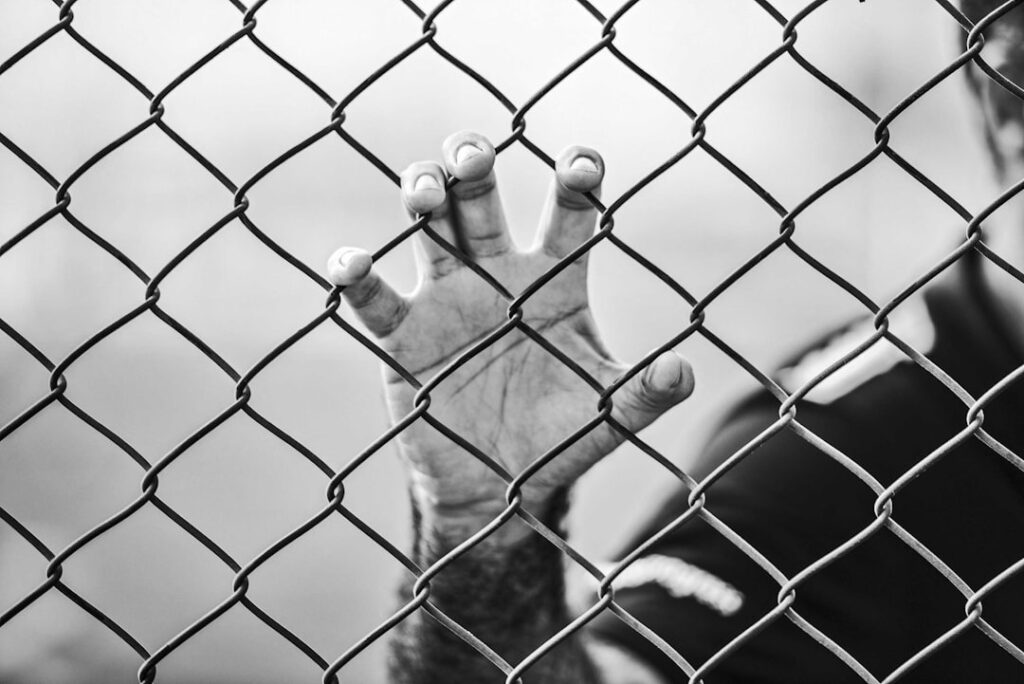 Main d'un prisonnier derrière une grille